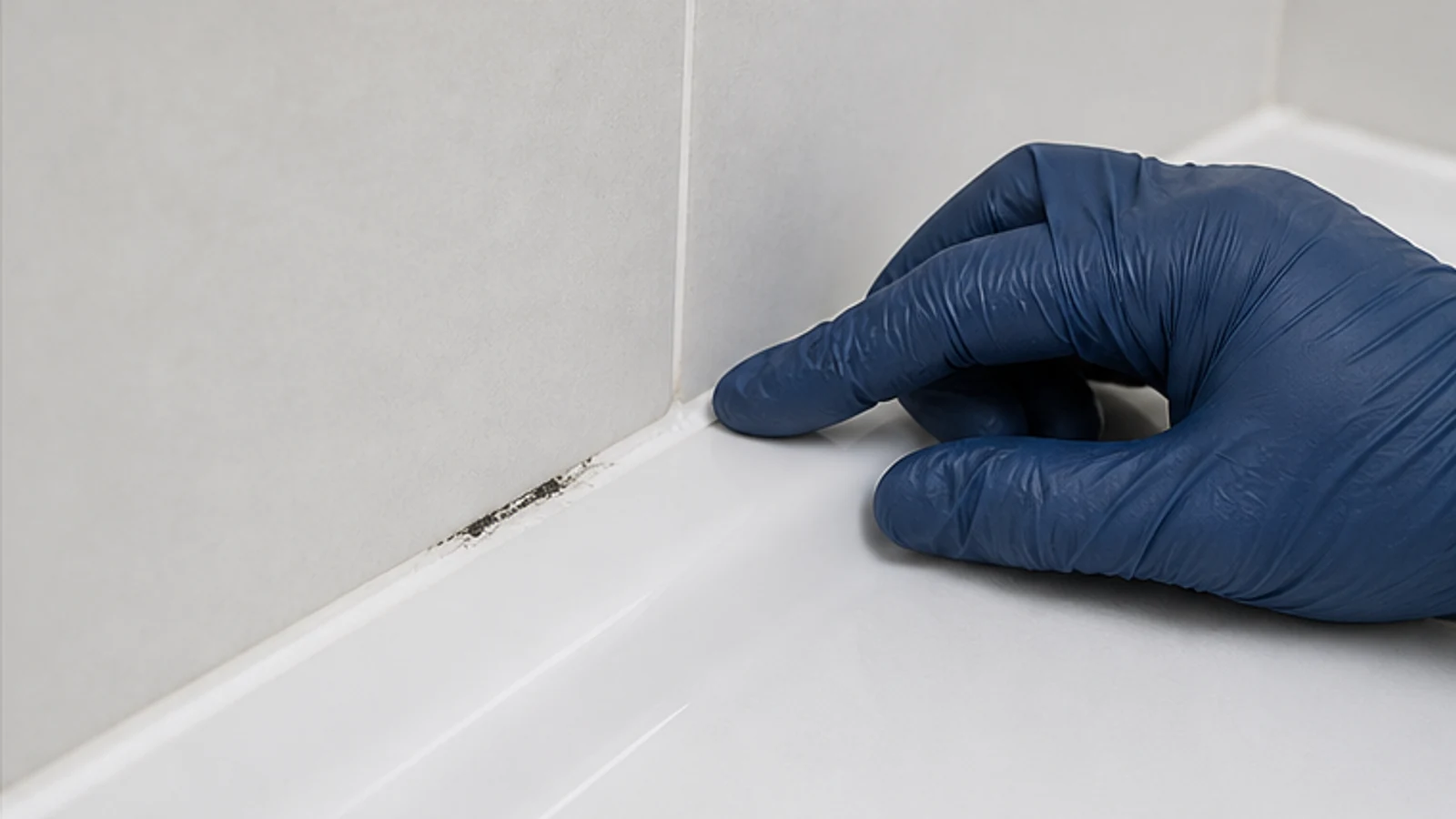 Gloved hand checking whether silicone sealant is firm and attached in a hidden shower corner