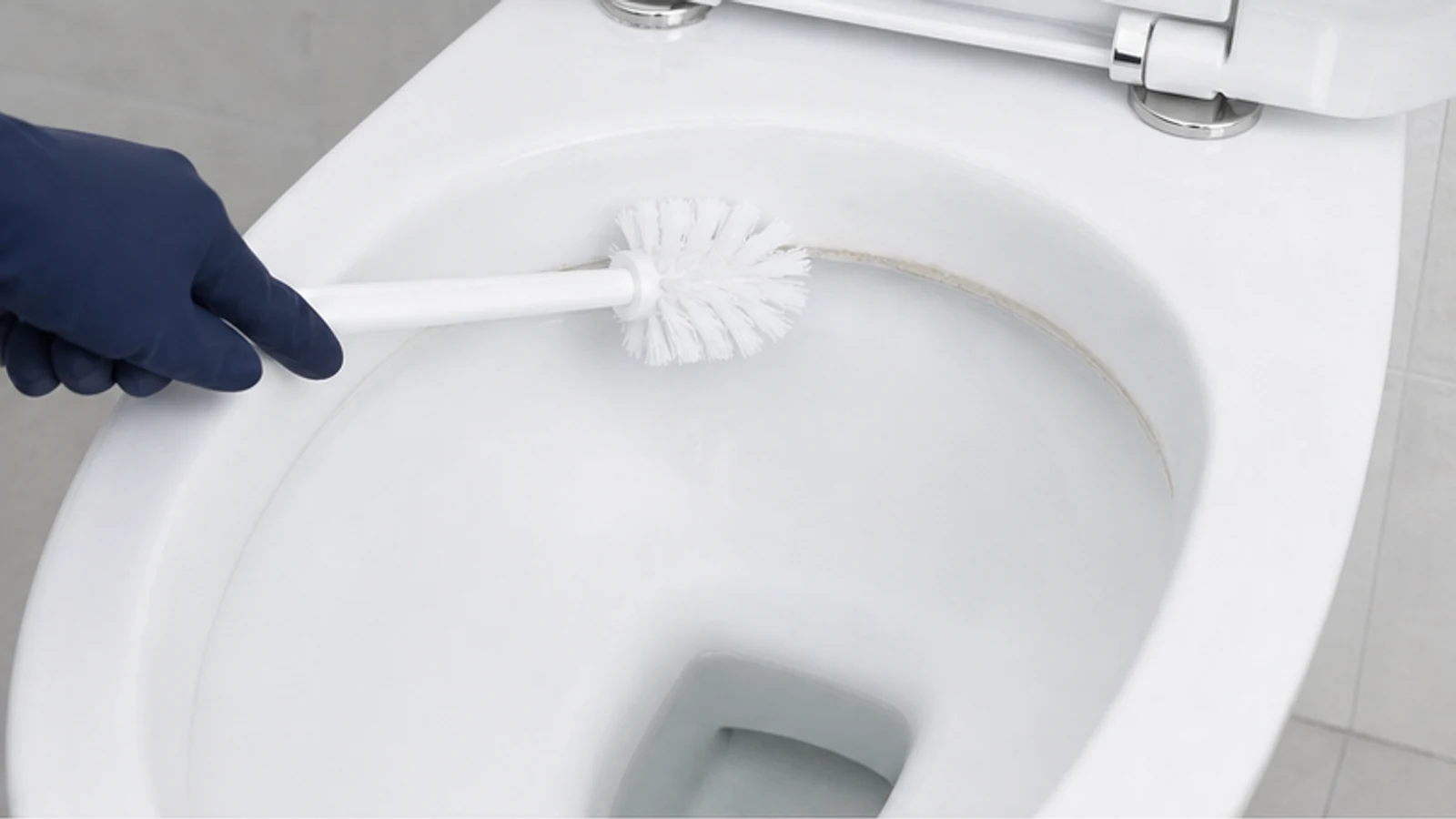 Gloved hand brushing a treated toilet-bowl ring gently with a nylon toilet brush