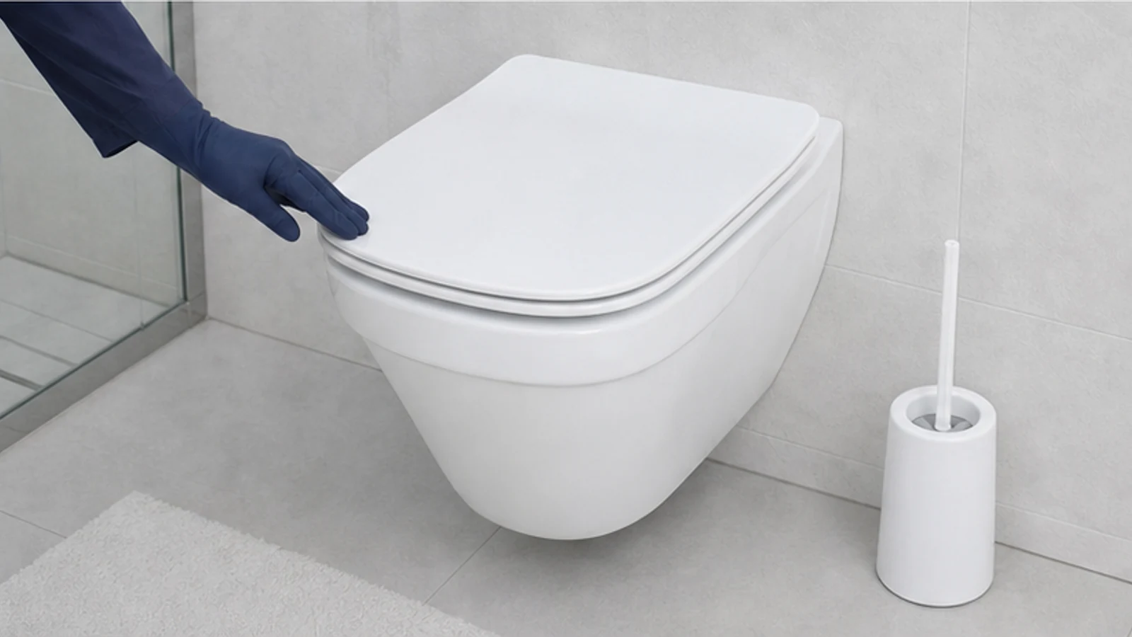 Gloved hand holding a toilet brush angled to scrub gently at the brown ring, circular motion visible, deposits beginning to lift.