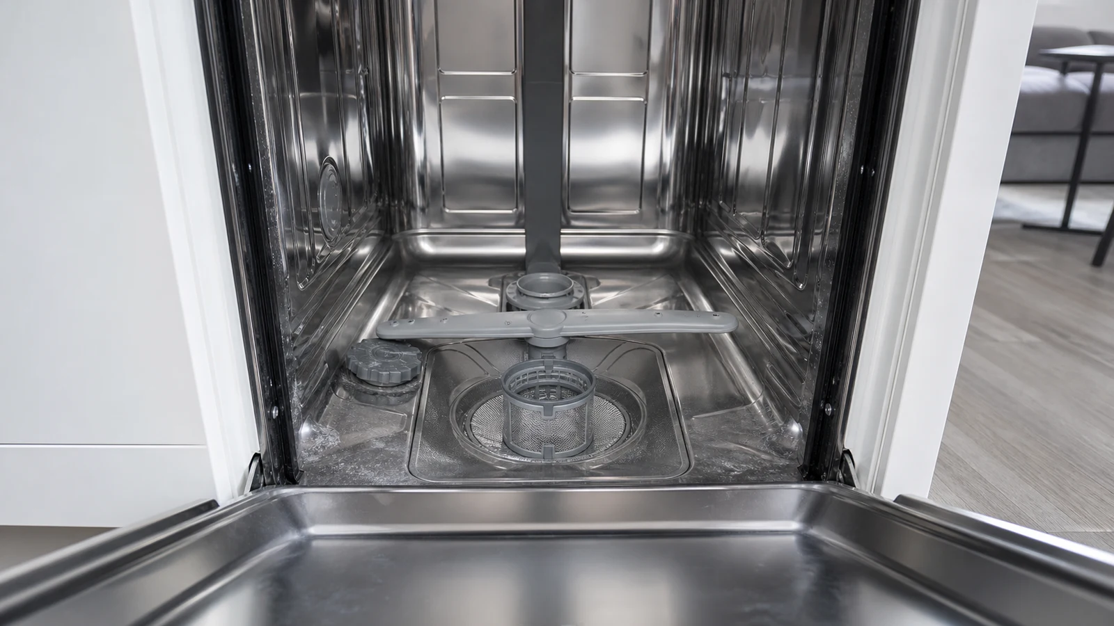 Interior view of a dishwasher showing the lower filter basket partially rotated and spray arms visible from above