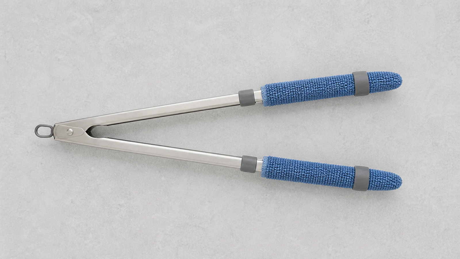 Pair of kitchen tongs laid flat with two microfibre cloths draped over each arm, secured with rubber bands near the handle and tips.