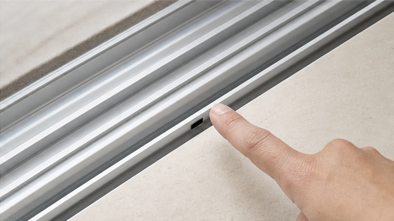 Finger pointing to the small adjustment screw recessed in the bottom rail of the sliding door panel.