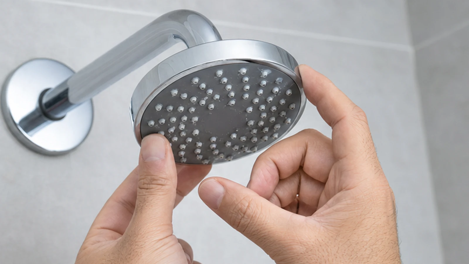 Hand checking the model mark beneath a chrome shower head before cleaning