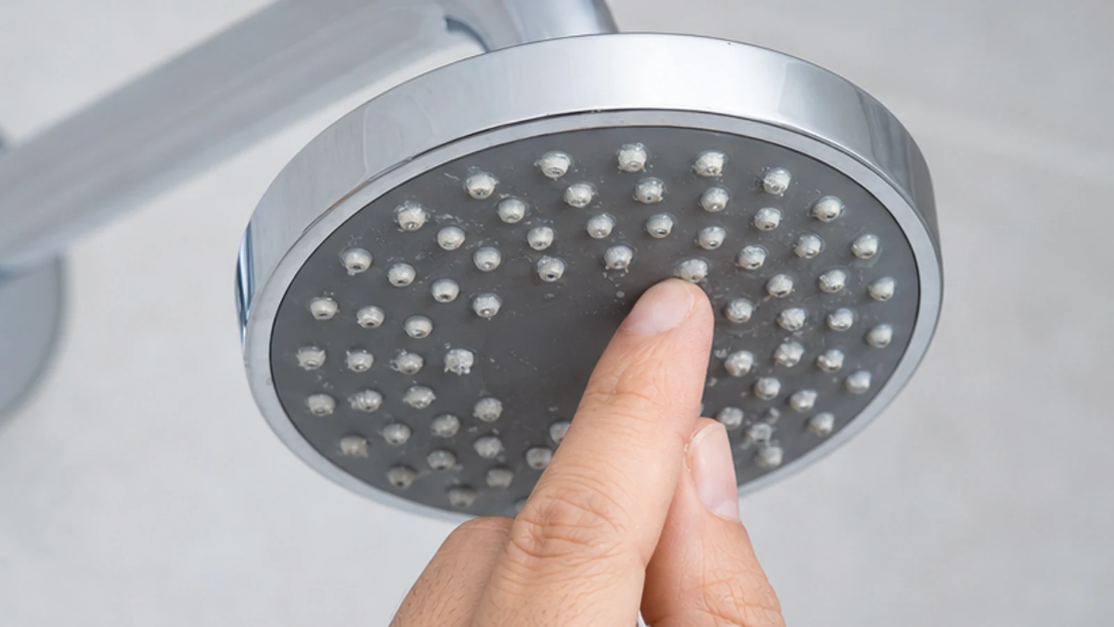 Hand gently rubbing flexible shower-head nozzles to release surface mineral deposits