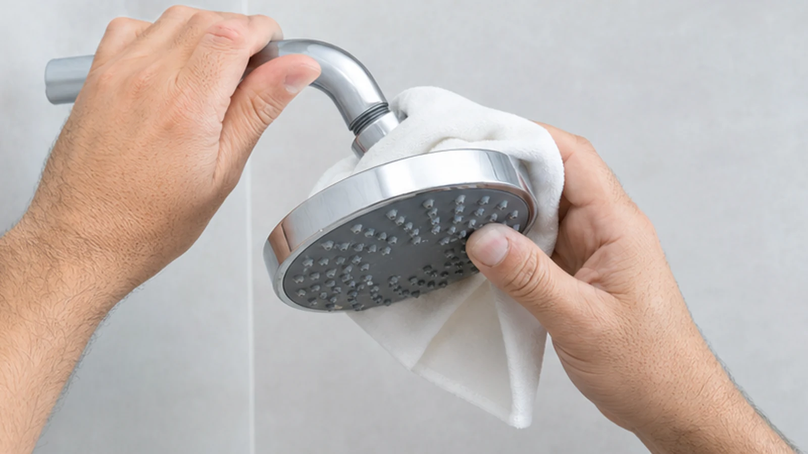 Two hands removing a compatible shower head by hand while supporting the shower arm