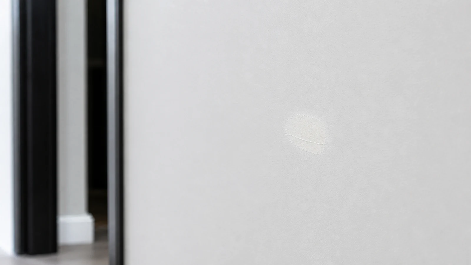 A fully dried, pale-white filled nail hole visible in painted wall surface, no longer wet, with feathered edges blending into the wall.