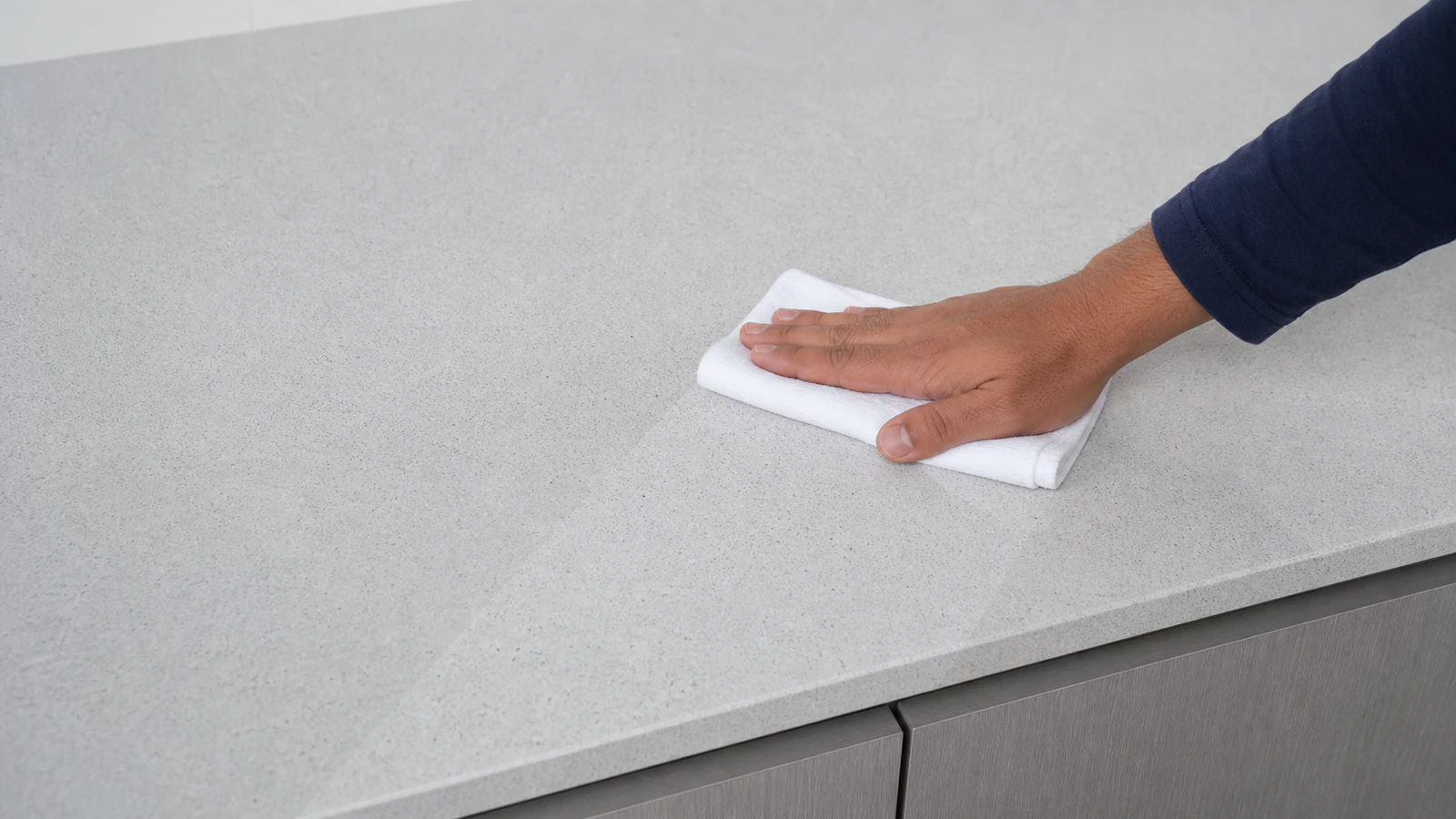 A hand using a dry, light-coloured cotton cloth to wipe the final moisture from a countertop, with natural light showing the sheen.