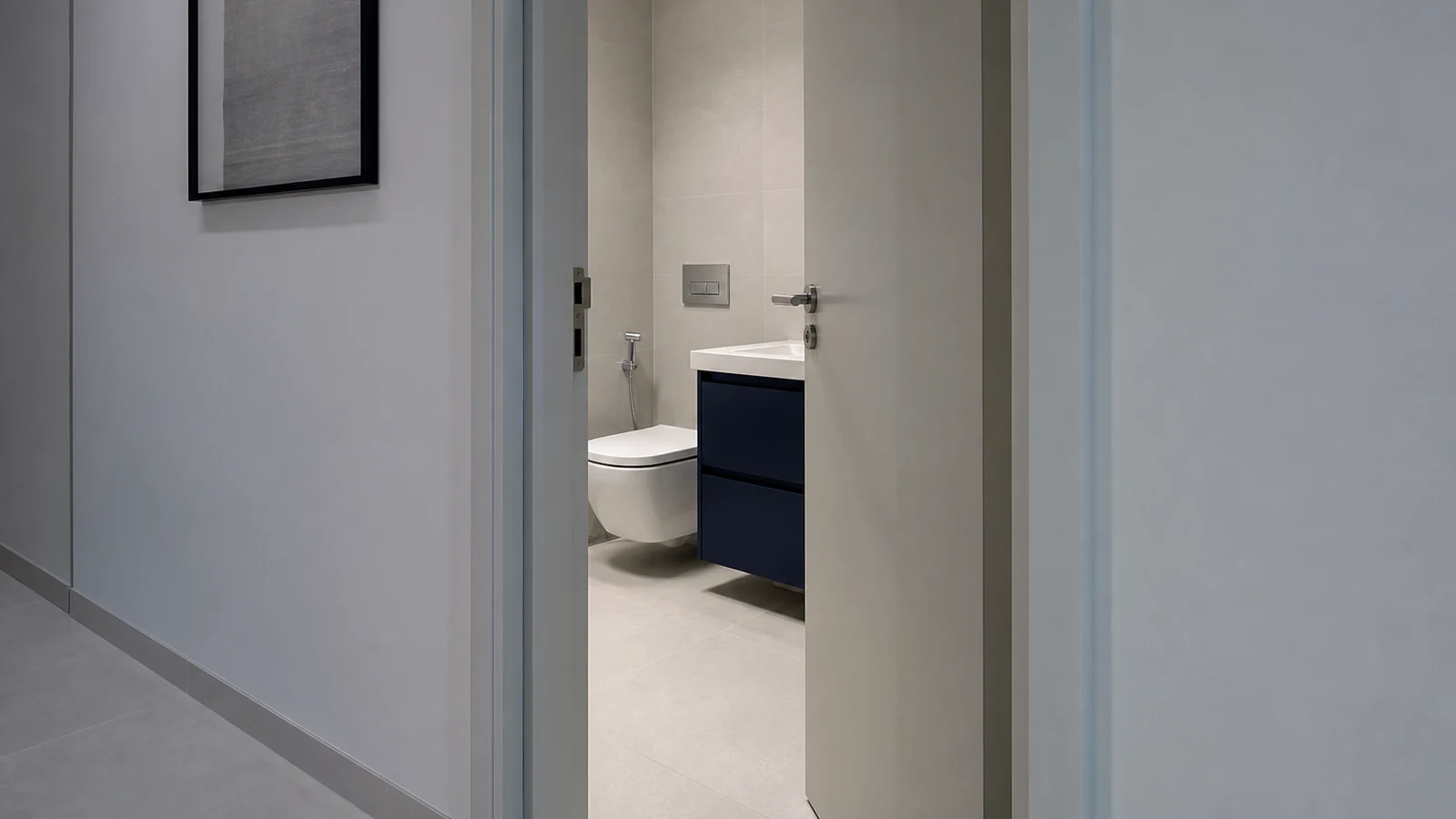 Partial view of a bathroom doorway open by 15 cm, showing the bathroom interior and daylit hallway, contemporary UAE apartment.