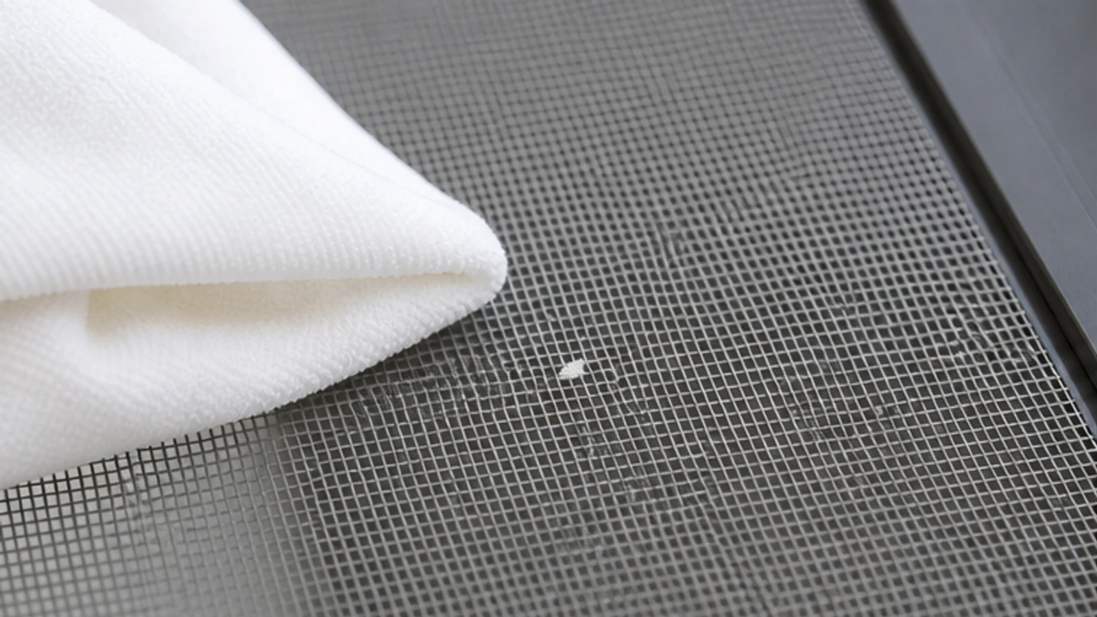 A barely damp soft cloth touching one fresh water-based paint speck on supported screen mesh.