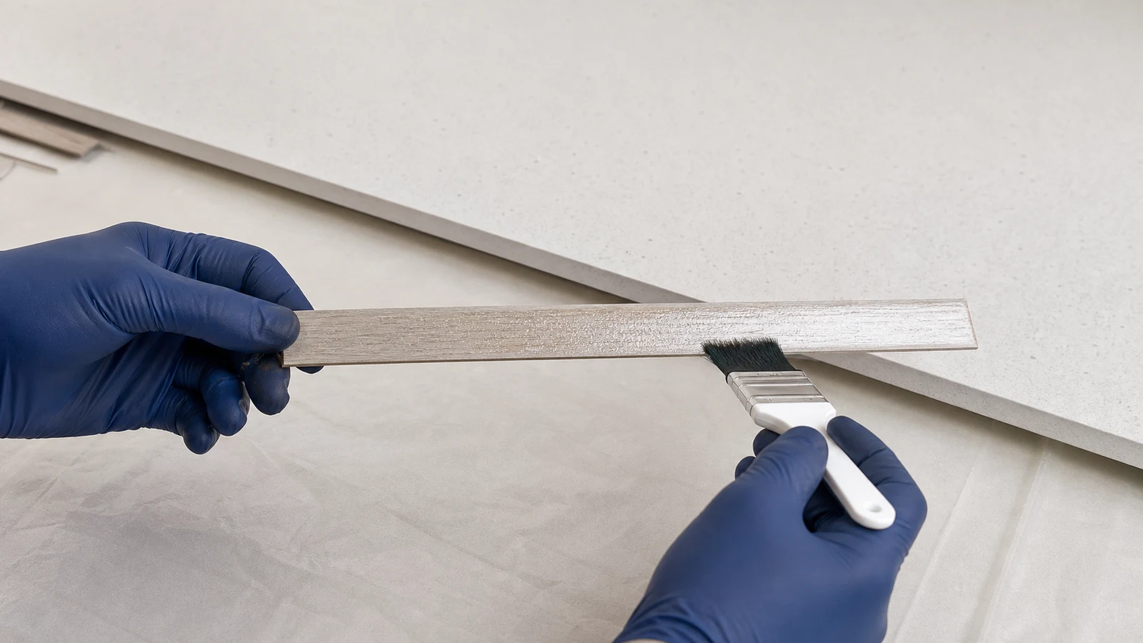A brush applying contact adhesive to the back surface of a laminate edge strip.