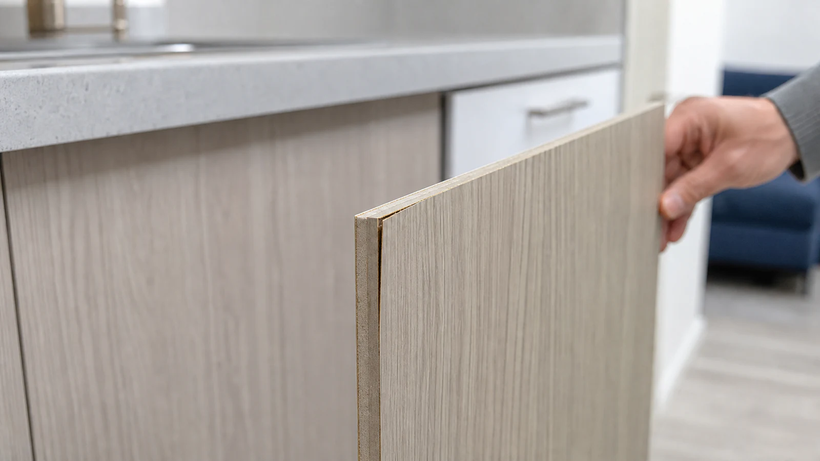 Close-up of a cabinet door corner where natural veneer is lifting slightly away from the substrate, visible as a thin gap.