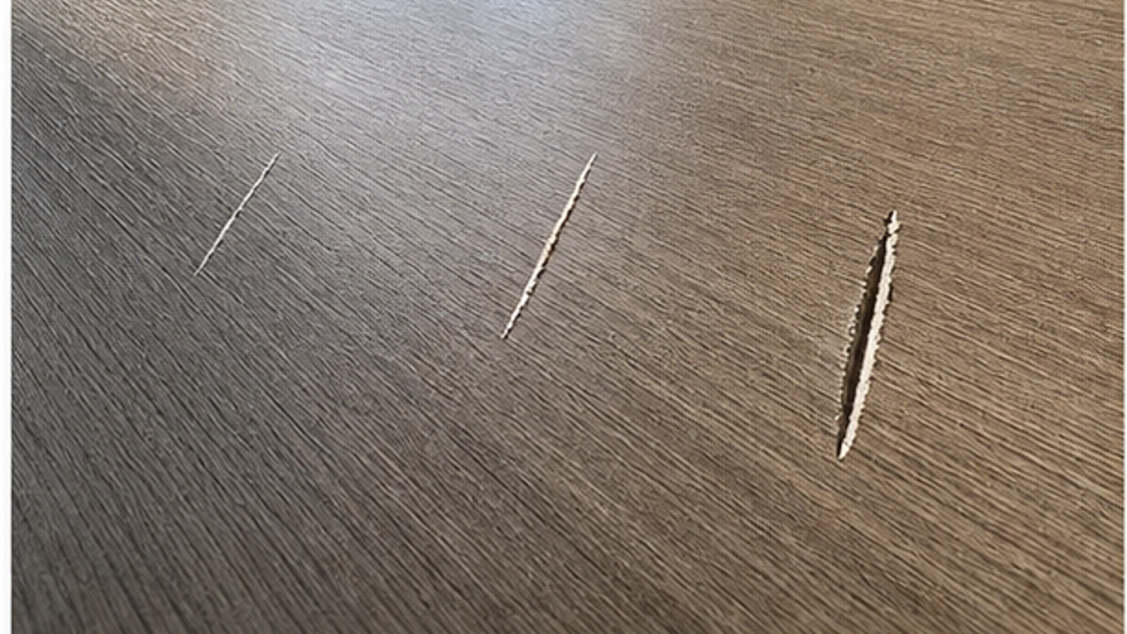 Three floor scratches of increasing depth shown in side light for visual diagnosis, with no repair products applied.