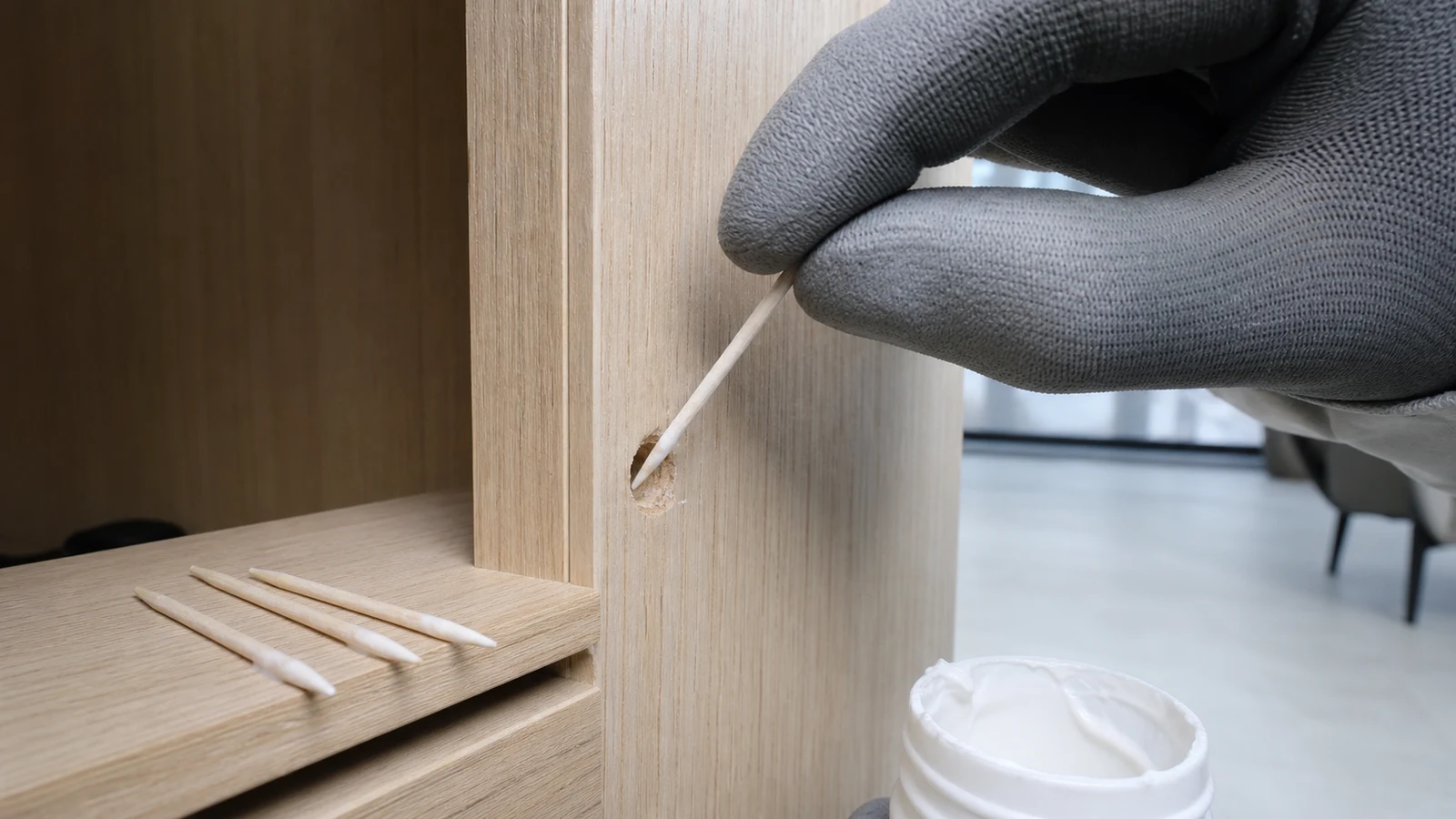 Four wooden toothpicks lightly coated with white wood glue are positioned at a stripped screw hole in a cabinet door.