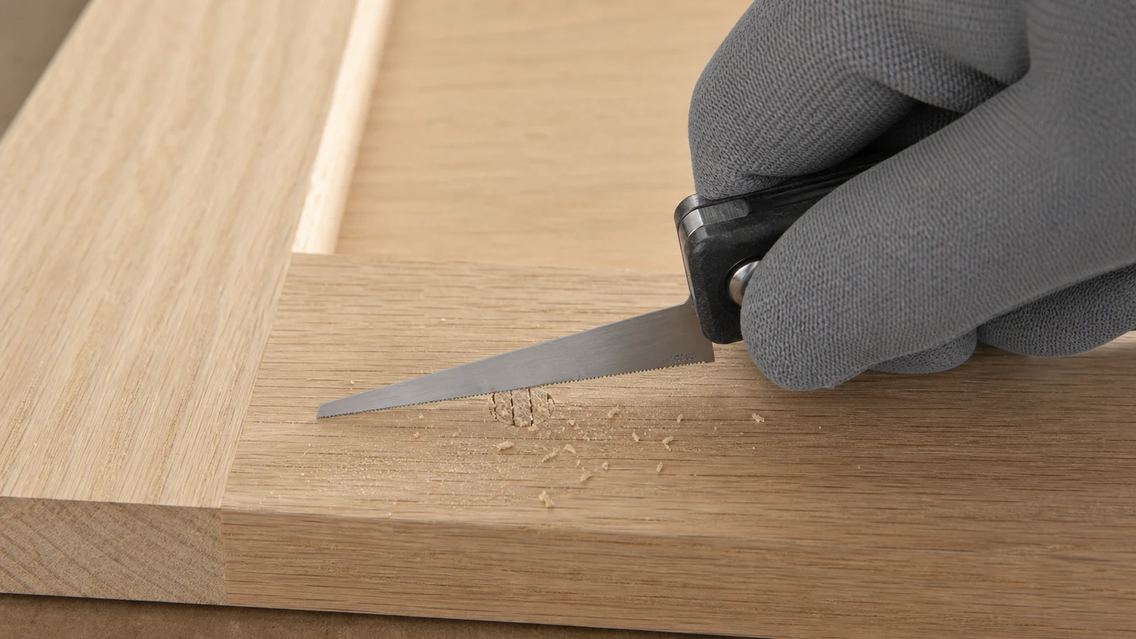 A fine handsaw cutting flush across the top of four cured toothpicks protruding from a screw hole, the saw blade parallel to the wood surface.