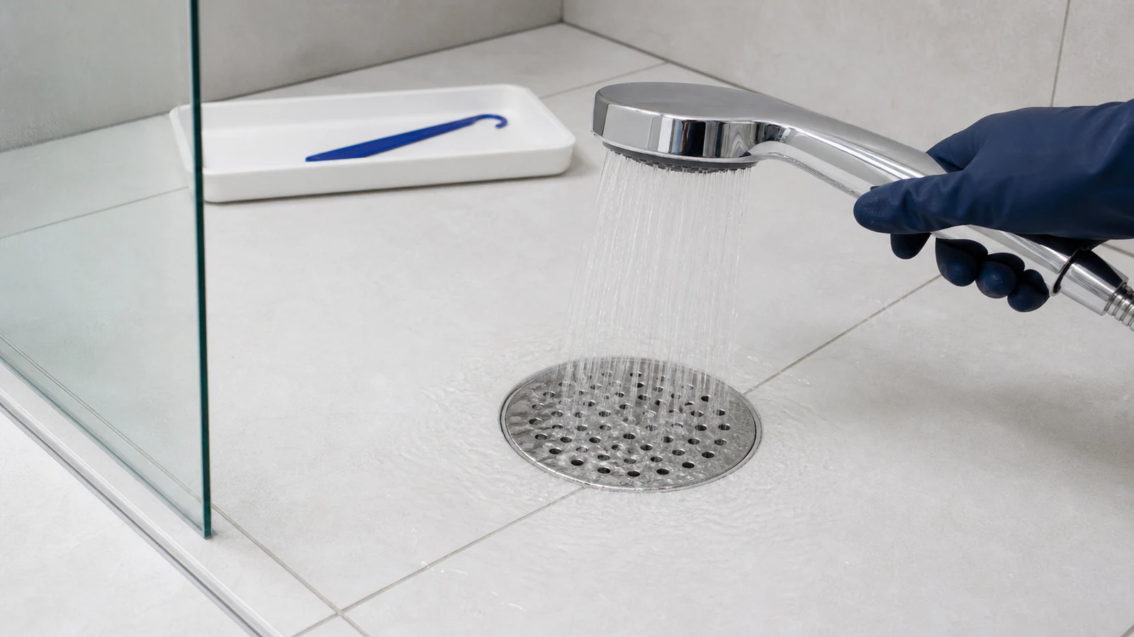 Water flowing freely down an open drain cavity while a gloved hand holds the plastic hook nearby, at the ready.