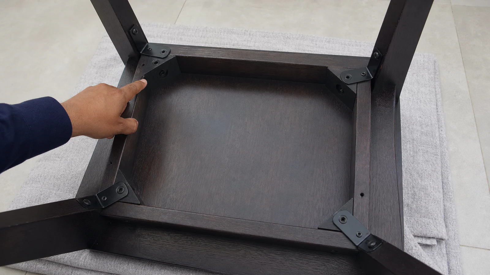 Upturned wooden chair showing multiple fasteners where legs attach to the seat frame, natural indoor daylight.